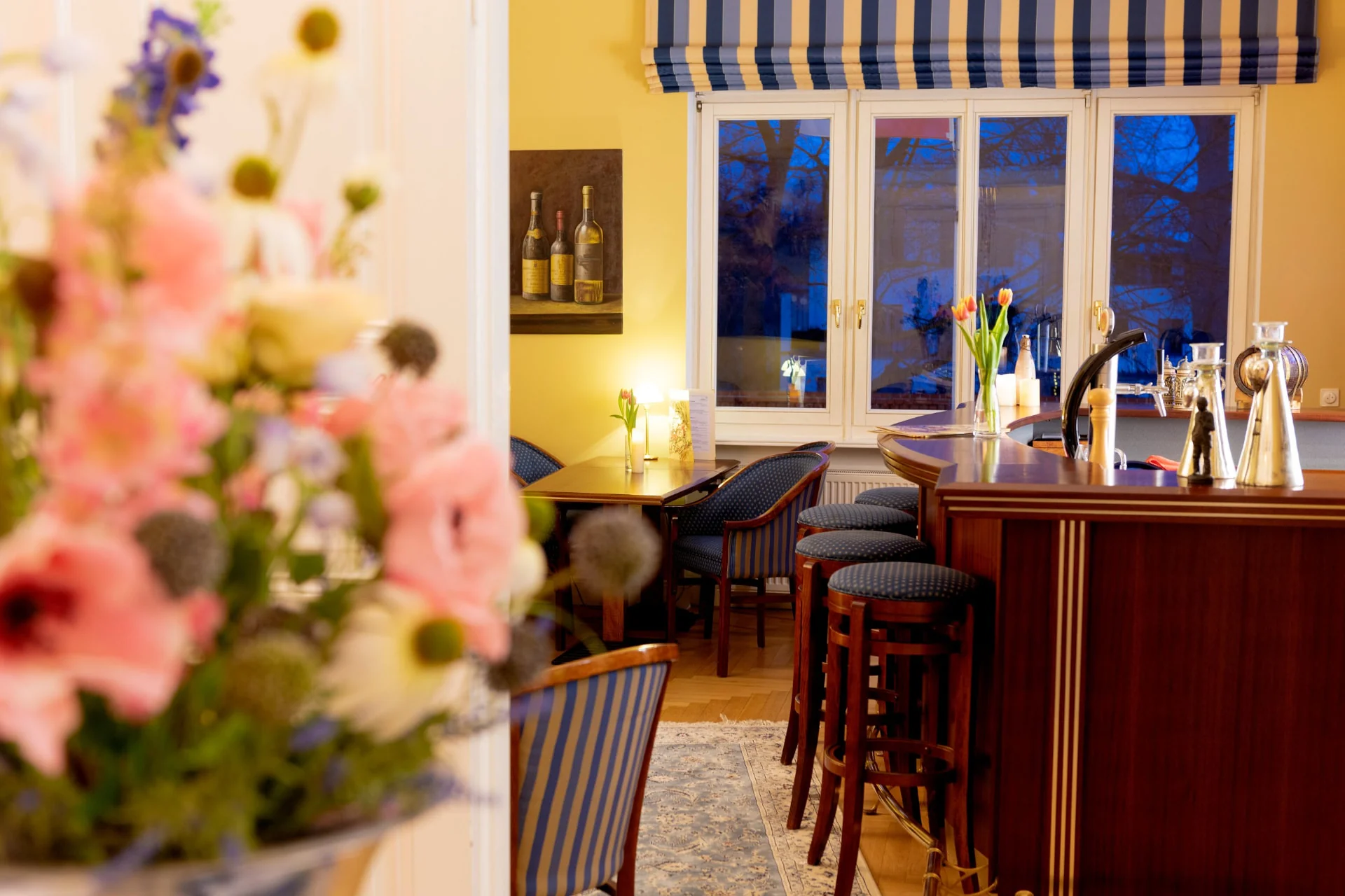 Blick in die Hotelbar mit Blumenstrauß, Barhockern und Bistrotischen